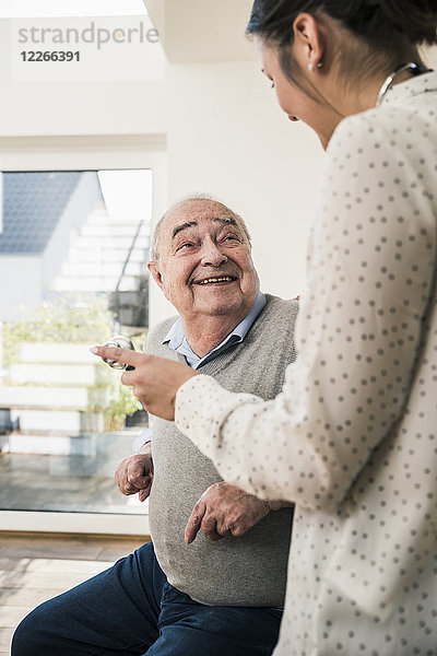 Älterer Mann lächelt Krankenschwester mit Stethoskop zu Hause an