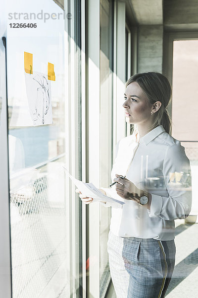 Junge Geschäftsfrau schaut auf Papier am Fenster