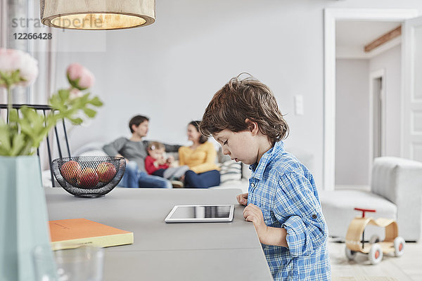 Junge schaut zu Hause mit Familie im Hintergrund auf die Tablette
