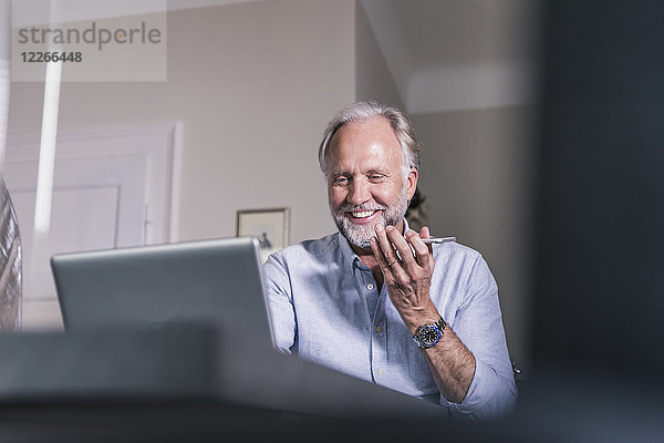 Porträt des lächelnden reifen Mannes mit Laptop und Handy zu Hause
