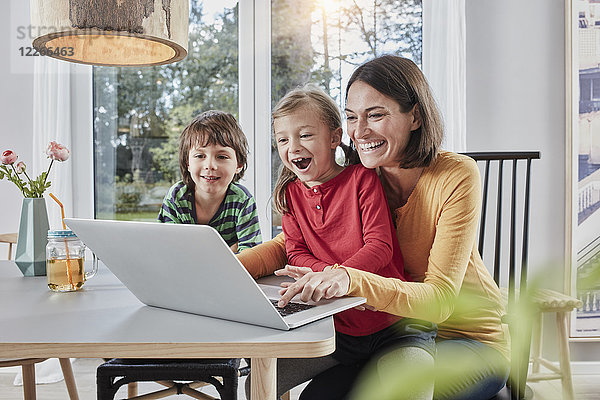 Glückliche Mutter mit zwei Kindern mit Laptop zu Hause