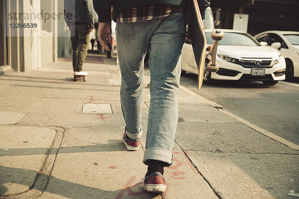 Niedriger Abschnitt des Mannes  der auf dem Bürgersteig mit Skateboard läuft.