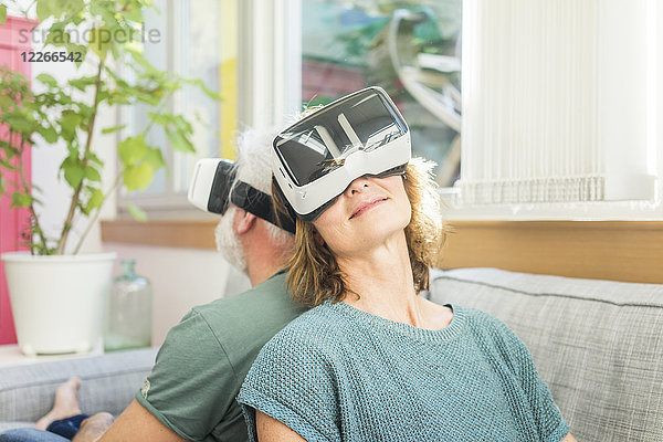 Erwachsenes Paar  das zu Hause auf der Couch sitzt und eine VR-Brille trägt.