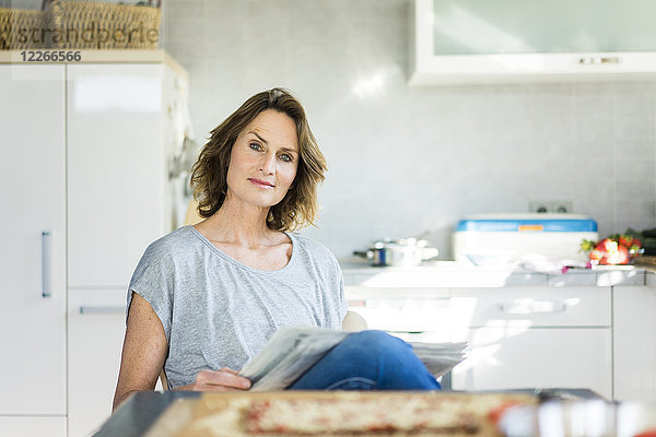 Porträt einer Frau mit Zeitung in der Küche zu Hause