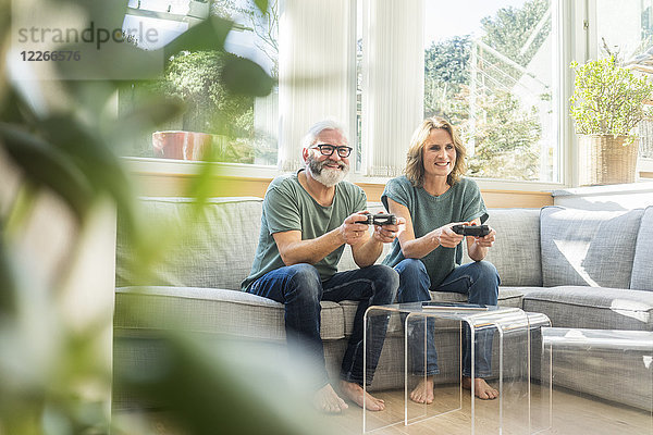 Glückliches reifes Paar  das zu Hause auf der Couch sitzt und Videospiele spielt.