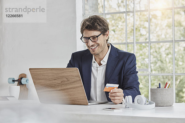 Lächelnder Geschäftsmann mit Laptop auf Schreibtisch-Haltekarte