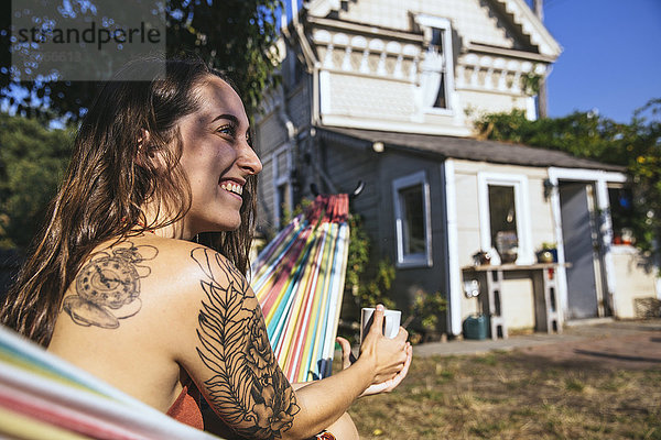 Glückliche junge Frau mit Tattoo in Hängematte