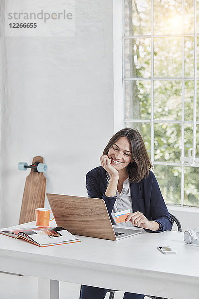 Lächelnde Geschäftsfrau mit Laptop auf Schreibtisch-Haltekarte