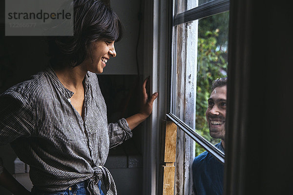Ein glückliches Paar lächelt sich durchs Fenster an.