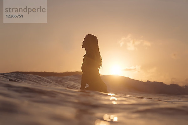 Indonesien  Lombok  Surferin bei Sonnenuntergang auf dem Surfbrett sitzend