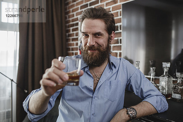 Porträt eines lächelnden Mannes mit einem Glas Whiskey zu Hause