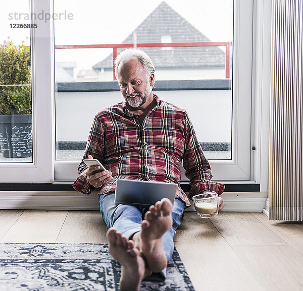 Lächelnder Mann entspannt sich zu Hause auf dem Boden mit Laptop und einer Tasse weißem Kaffee.