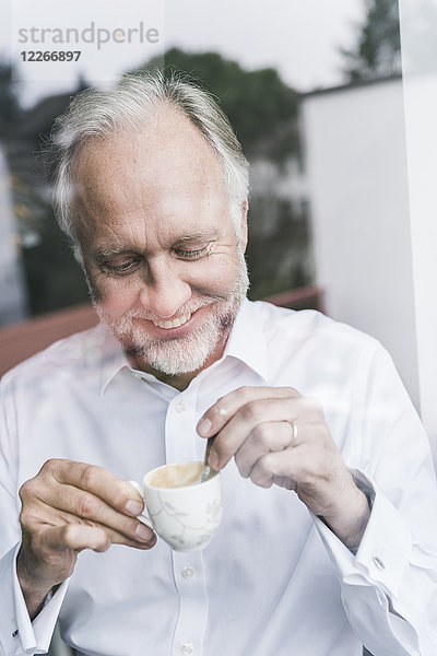 Porträt eines glücklichen reifen Mannes hinter einer Glasscheibe mit einer Tasse Espresso