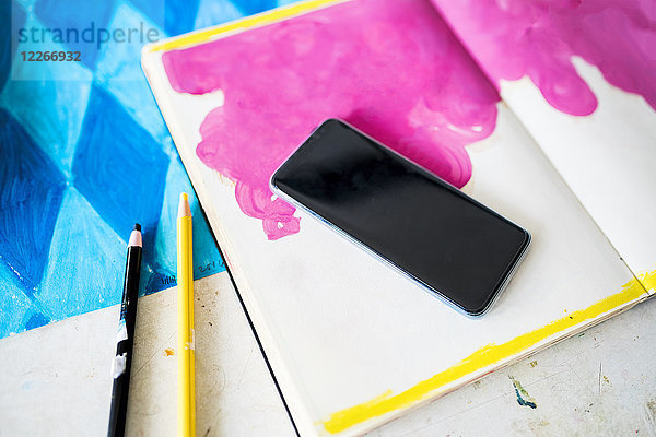 Smartphone liegend auf einem Notebook mit rosa Zeichnung im Atelier des Künstlers