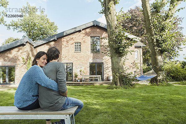 Lächelndes  liebevolles Paar  das im Garten seines Hauses sitzt.