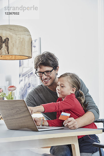 Glückliche Vater und Tochter mit einer Karte mit Laptop auf dem Tisch zu Hause