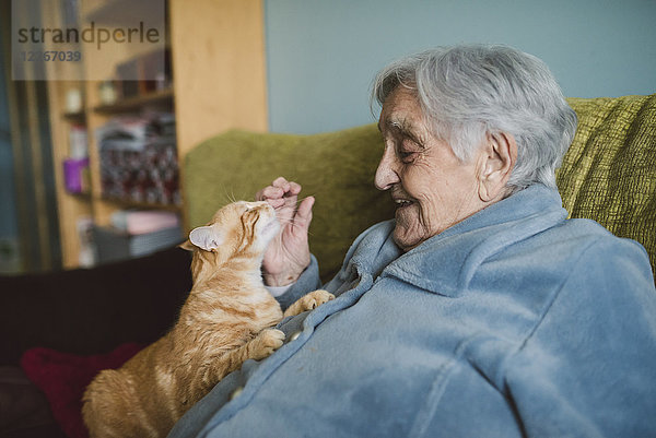 Fröhliche Seniorin mit Tabbykatze auf der Couch