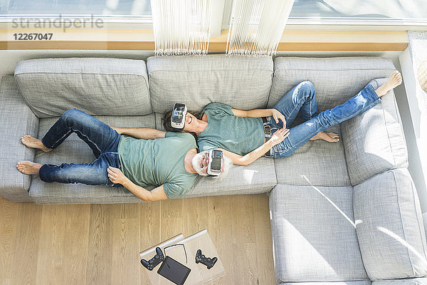 Glückliches reifes Paar  das zu Hause auf der Couch liegt und eine VR-Brille trägt.