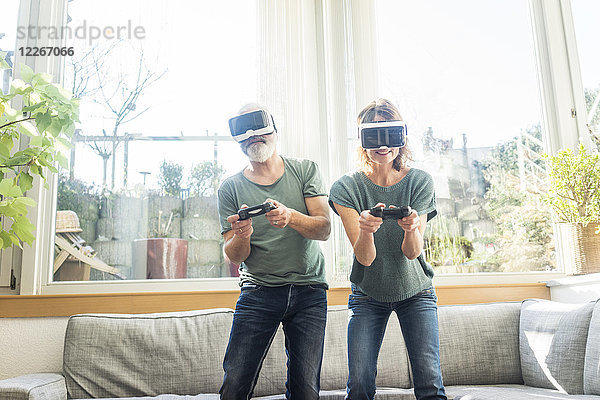 Erwachsenes Paar im Wohnzimmer zu Hause mit VR-Brille beim Videospielen