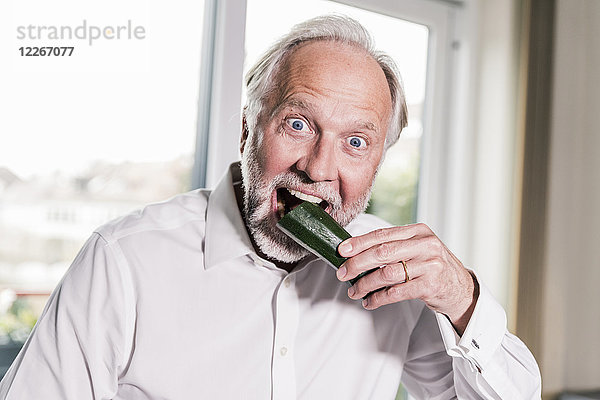 Porträt eines reifen Mannes  der in Zucchini beißt