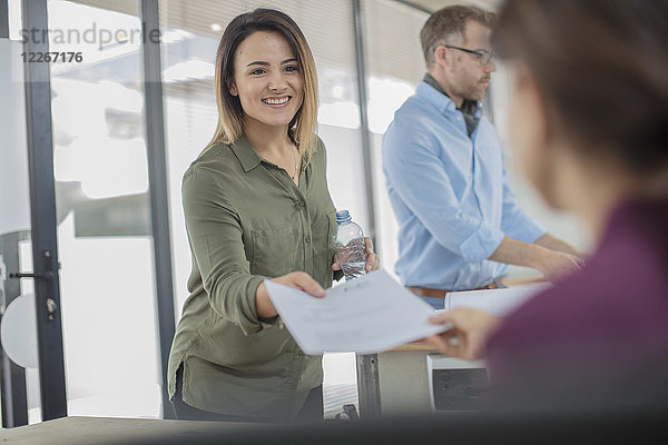 Lächelnde Geschäftsfrau im Büro übergibt Papier an Kollegen