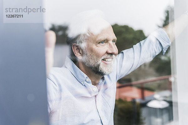 Porträt eines glücklichen  reifen Mannes  der aus der Fensterscheibe schaut.
