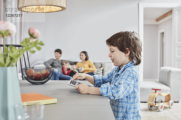 Junge schaut zu Hause mit Familie im Hintergrund auf die Tablette