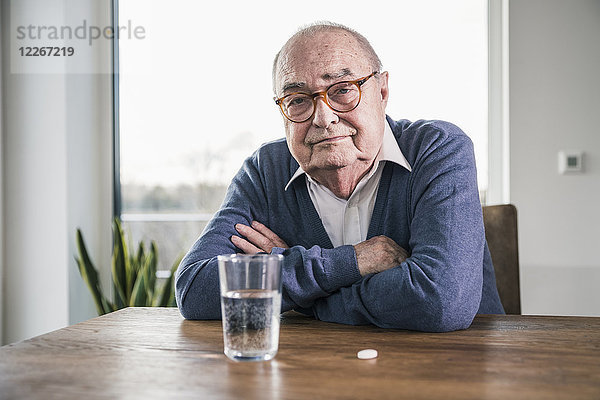 Porträt eines älteren Mannes am Tisch mit Pille und Wasserglas