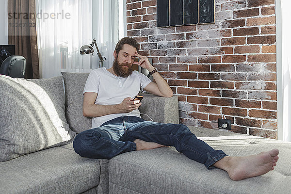 Mann mit Handy entspannt auf der Couch zu Hause