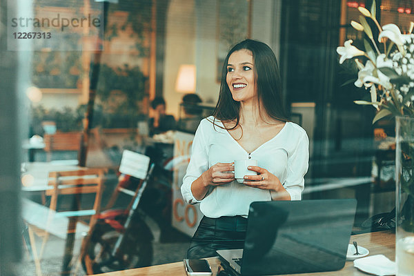Porträt einer lachenden jungen Frau  die in einem Coffee-Shop wartet.