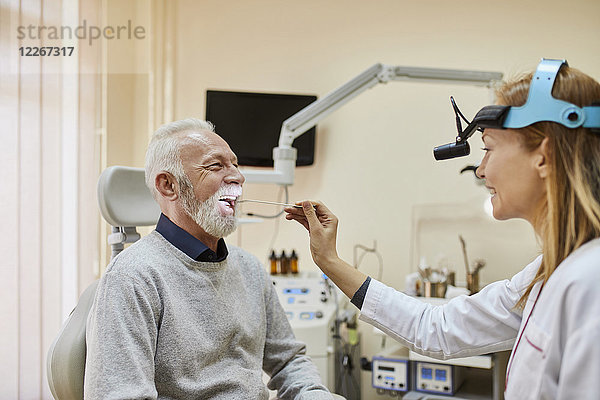 HNO-Arzt untersucht Mund eines älteren Mannes