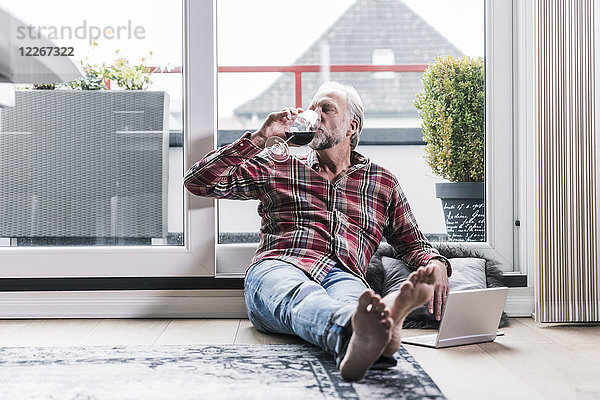 Barfuss-Mann entspannt sich zu Hause auf dem Boden und trinkt ein Glas Rotwein.