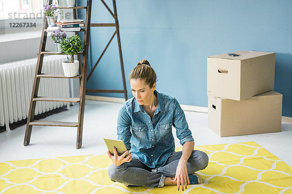 Frau sitzt auf dem Boden ihrer neuen Wohnung  mit Hilfe eines digitalen Tabletts.