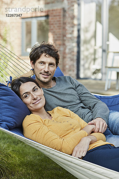 Lächelndes Paar in der Hängematte im Garten des Hauses liegend
