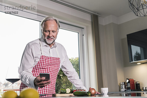 Portrait des reifen Mannes in der Küche mit dem Handy