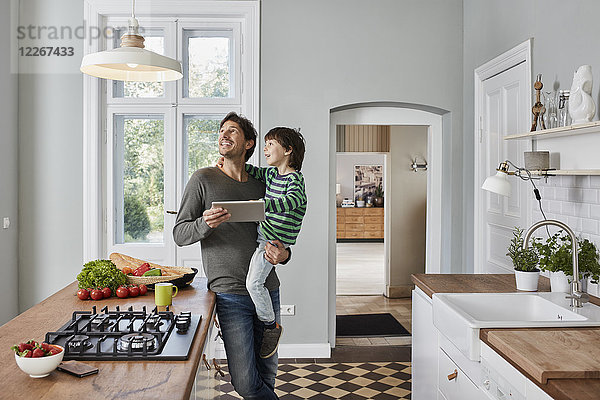 Vater und Sohn mit Tablette in der Küche mit Blick auf die Deckenlampe