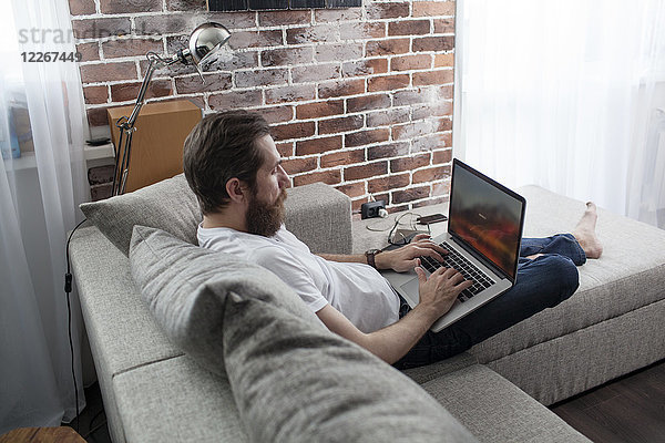 Mann sitzt auf der Couch zu Hause mit Laptop