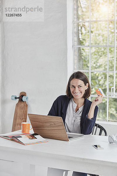 Lächelnde Geschäftsfrau mit Laptop auf Schreibtisch-Haltekarte