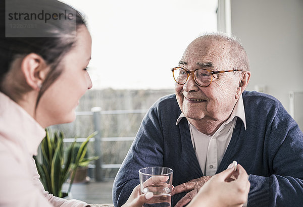 Frau hält Pille und Glas Wasser für lächelnden älteren Mann