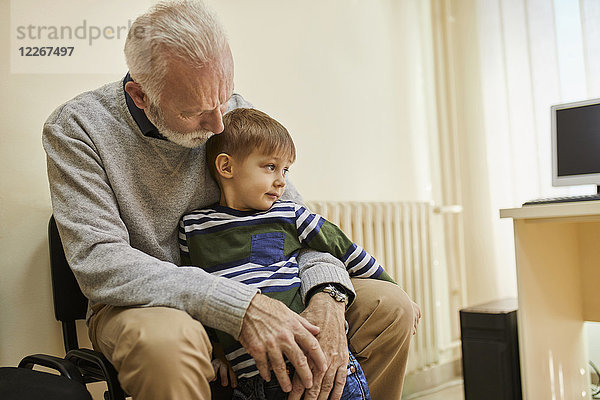 Junge sitzt auf Großvaters Schoß im Wartezimmer