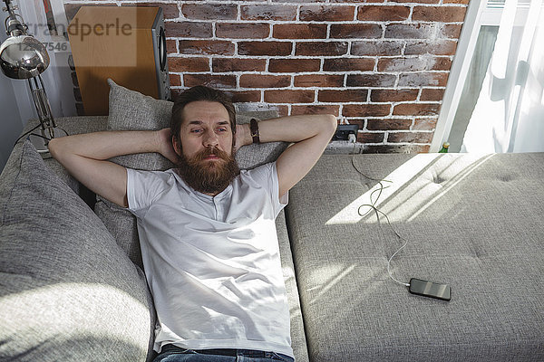 Porträt eines bärtigen Mannes  der sich zu Hause auf der Couch entspannt.