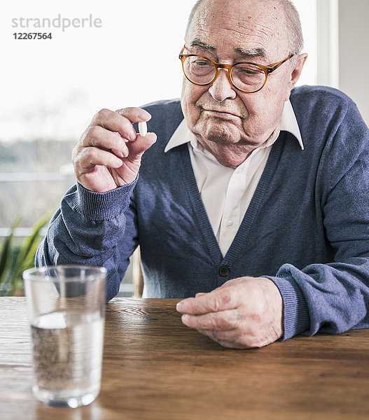 Porträt eines älteren Mannes am Tisch mit Pille und Wasserglas