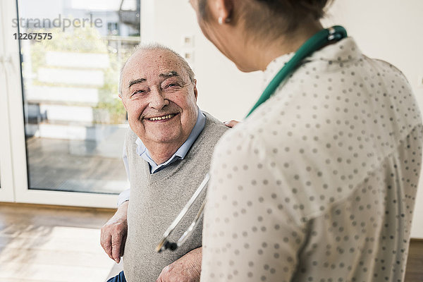 Älterer Mann lächelt Krankenschwester zu Hause an.