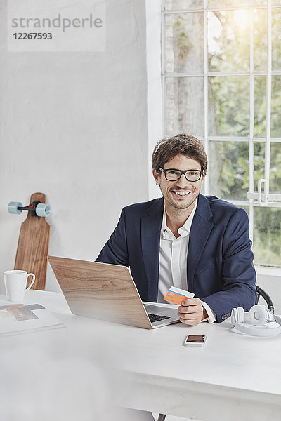 Porträt eines lächelnden Geschäftsmannes mit Laptop auf Schreibtisch-Haltekarte