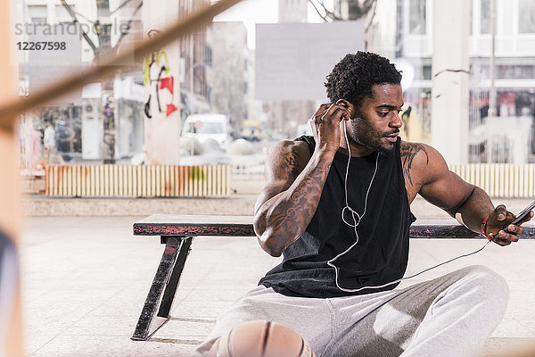 Mann mit Tattoos und Basketball über Smartphone und Kopfhörer