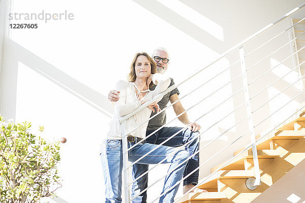 Porträt eines lächelnden  reifen Paares  das zu Hause auf einer Treppe steht.