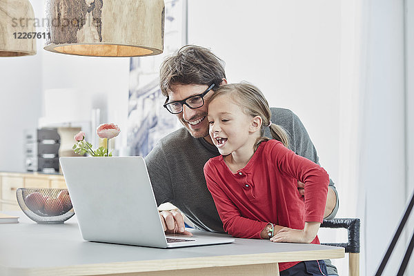Glücklicher Vater und Tochter mit Laptop auf dem Tisch zu Hause
