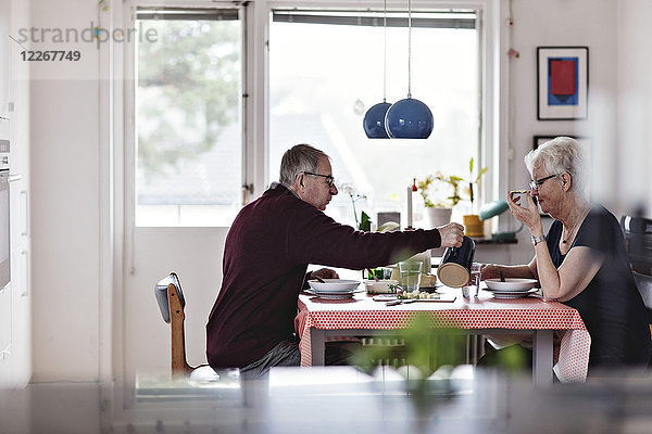 Seitenansicht des Seniorenpaares beim Essen am Esstisch gegen das Fenster