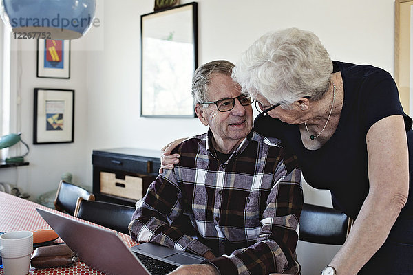 Lächelndes Seniorenpaar mit Laptop am Esstisch