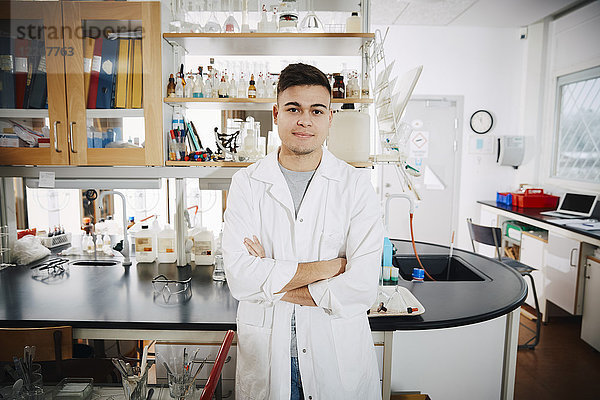 Porträt eines selbstbewussten jungen  männlichen Studenten mit gekreuzten Armen im Chemielabor